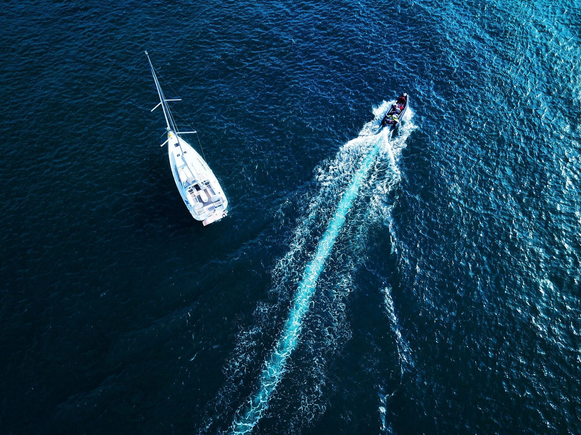 The image depicts a serene marina filled with various types of boats and super yachts. The water in the marina is calm, reflecting the clear, blue sky above. On the left side of the image, there is a cluster of smaller boats, which appear to be sailboats and pleasure crafts. Each of these boats is moored to wooden docks that stretch out into the water.
Towards the centre of the image, the size of the boats increases, transitioning to larger sailing yachts and motor yachts. These vessels have sleek, modern designs with white hulls that glisten under the sunlight.
To the right side of the image, the yachts reach an impressive scale, with several super yachts docked prominently. These luxurious vessels are equipped with multiple decks, expansive windows, and intricate details, showcasing their grandeur and opulence.
In the background, there's a picturesque landscape featuring lush green trees and hills, adding a natural frame to the marina. The overall atmosphere of the image is tranquil and reflective, capturing the elegance and lifestyle associated with maritime leisure and luxury.